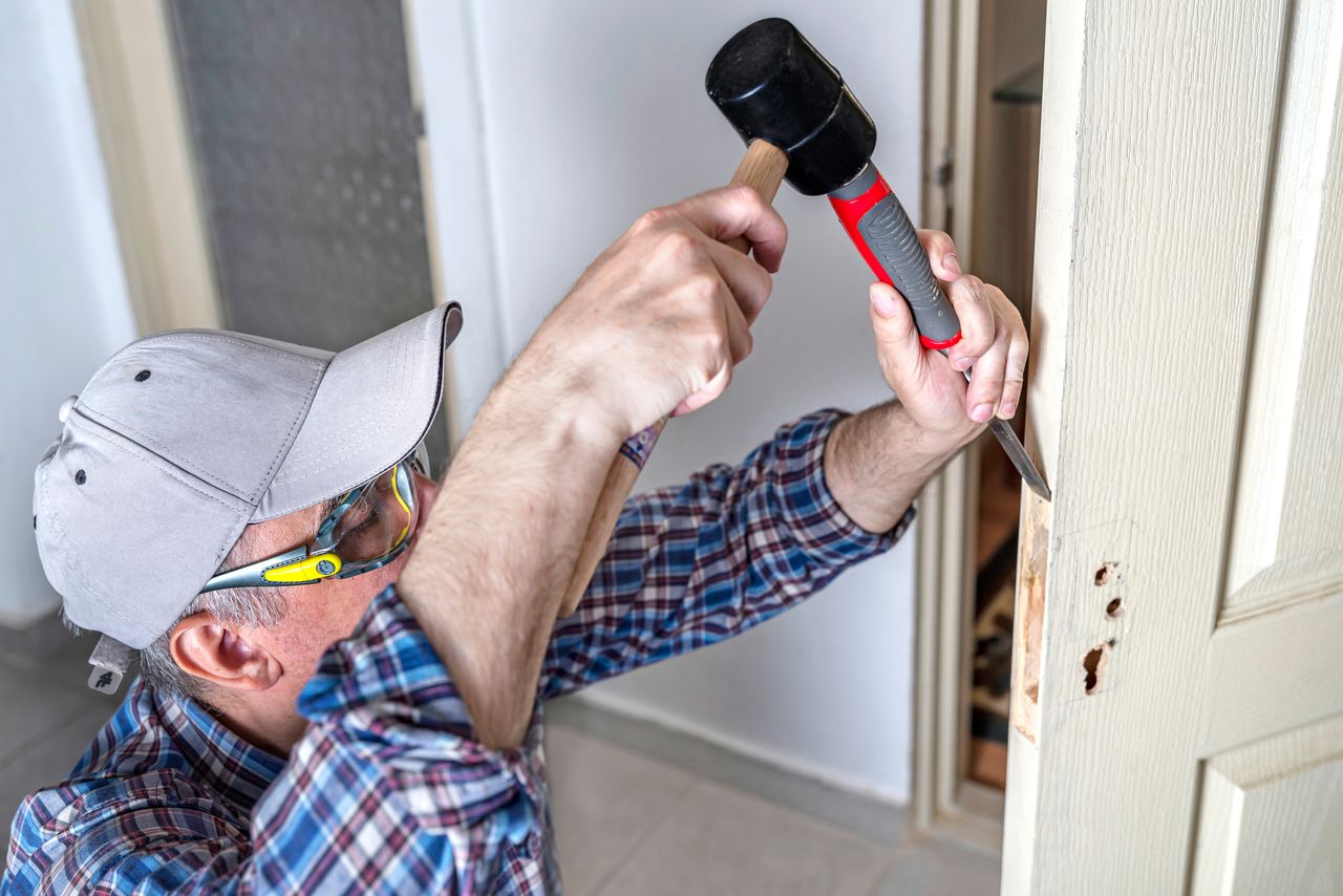 serrurier réalisant un encastrement pour la serrure à l'aide d'un ciseau à bois